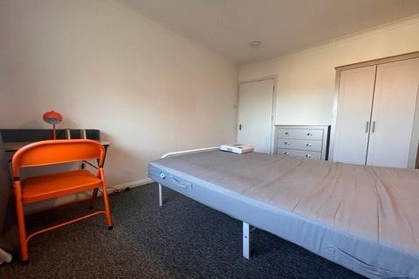 A cozy bedroom featuring a simple bed, a small ...