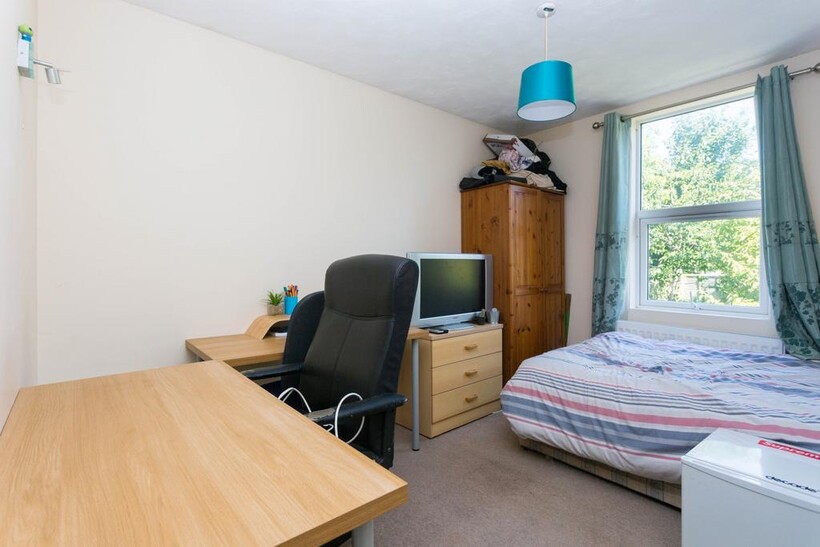 A well-lit bedroom featuring a bed, work desk, ...
